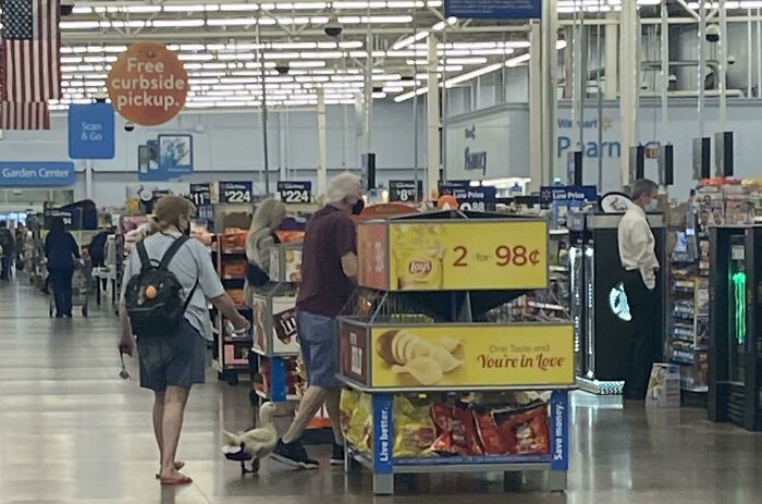 Zákazníci nakupujú chipsy v supermarkete, zľavy na Lay's 2 za 98 centov, letáky a svetlá v pozadí.