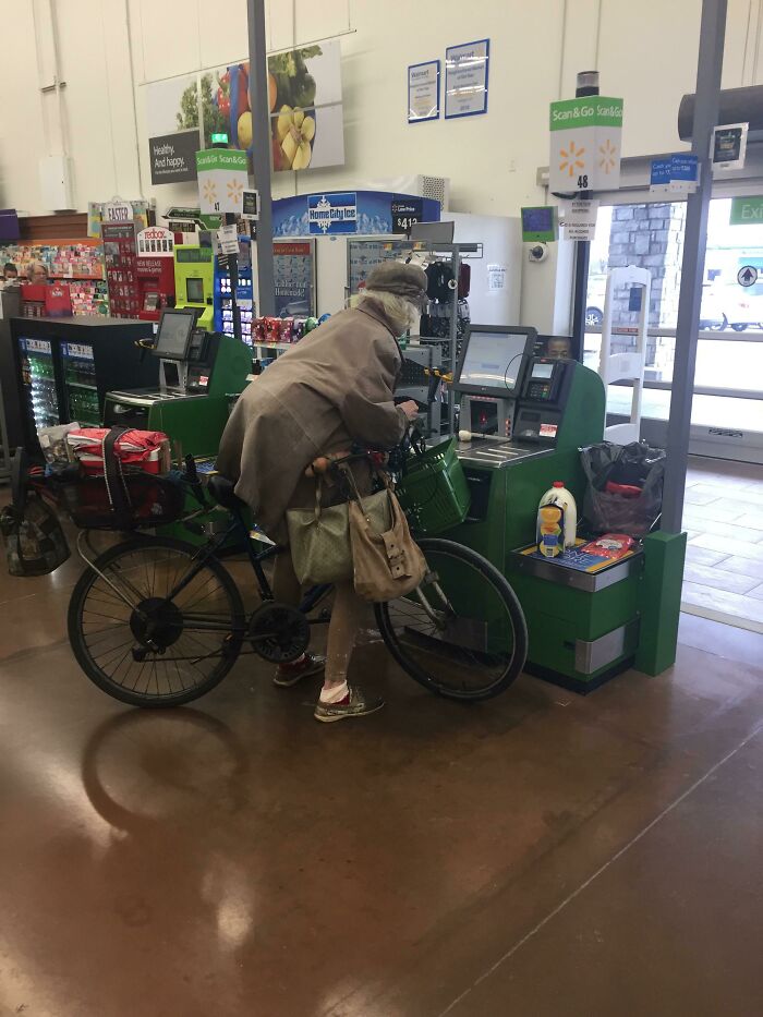 Osoba na bicykli pri samoobslužnej pokladni v obchode, skenuje nakúpené položky.