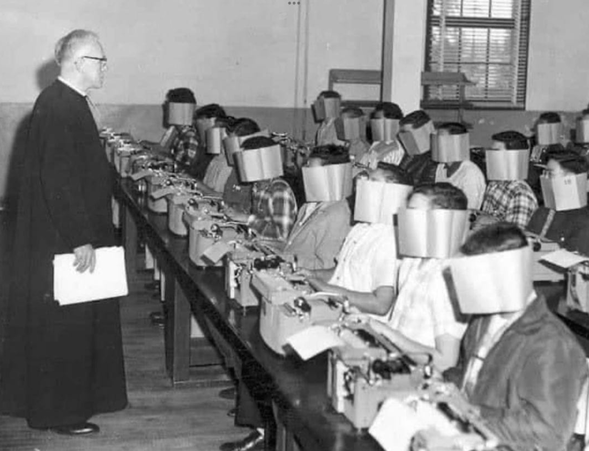 Historická učebňa písania na stroji so študentmi nosiacimi blokátory pohľadu, aby sa sústredili na zadania.