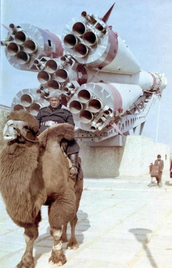 Muž na ťave pred obrovskou raketou na odpalovacej rampe, zachytávajúc kontrast starého a nového.