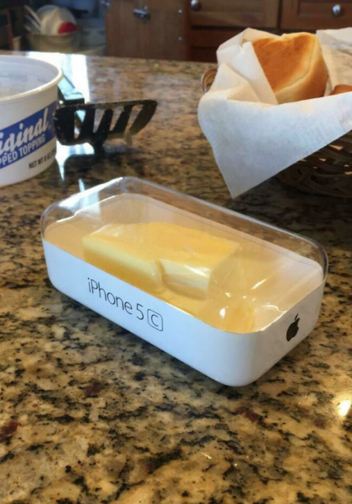 Maslo uložené v krabičke od iPhonu 5C na kuchynskej linke so sladkým pečivom v pozadí.
