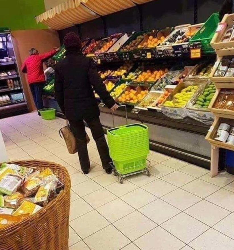 Nakupovanie ovocia v supermarkete, zákazníci s košíkom pri regáloch s čerstvým ovocím.