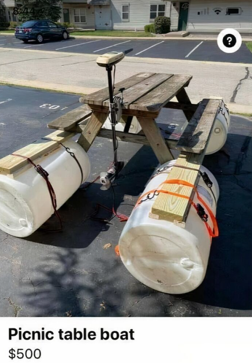 Piknikový stôl premenený na improvizovaný čln s plastovými sudmi a motorom, autentický dizajn na parkovisku.