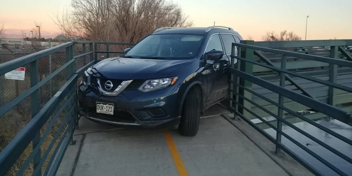 Auto uviaznuté medzi zábradlím na úzkom moste počas súmraku.
