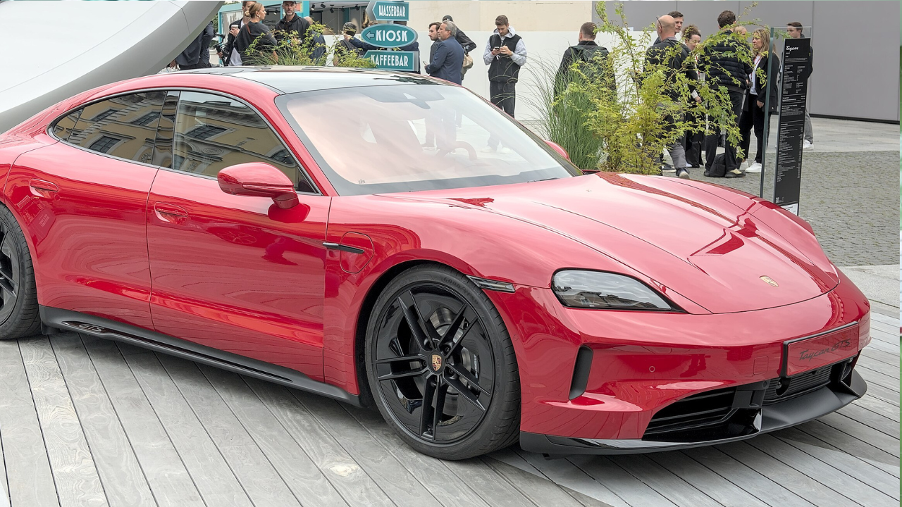 Červené športové auto Porsche Taycan zaparkované na výstave, obklopené ľuďmi.