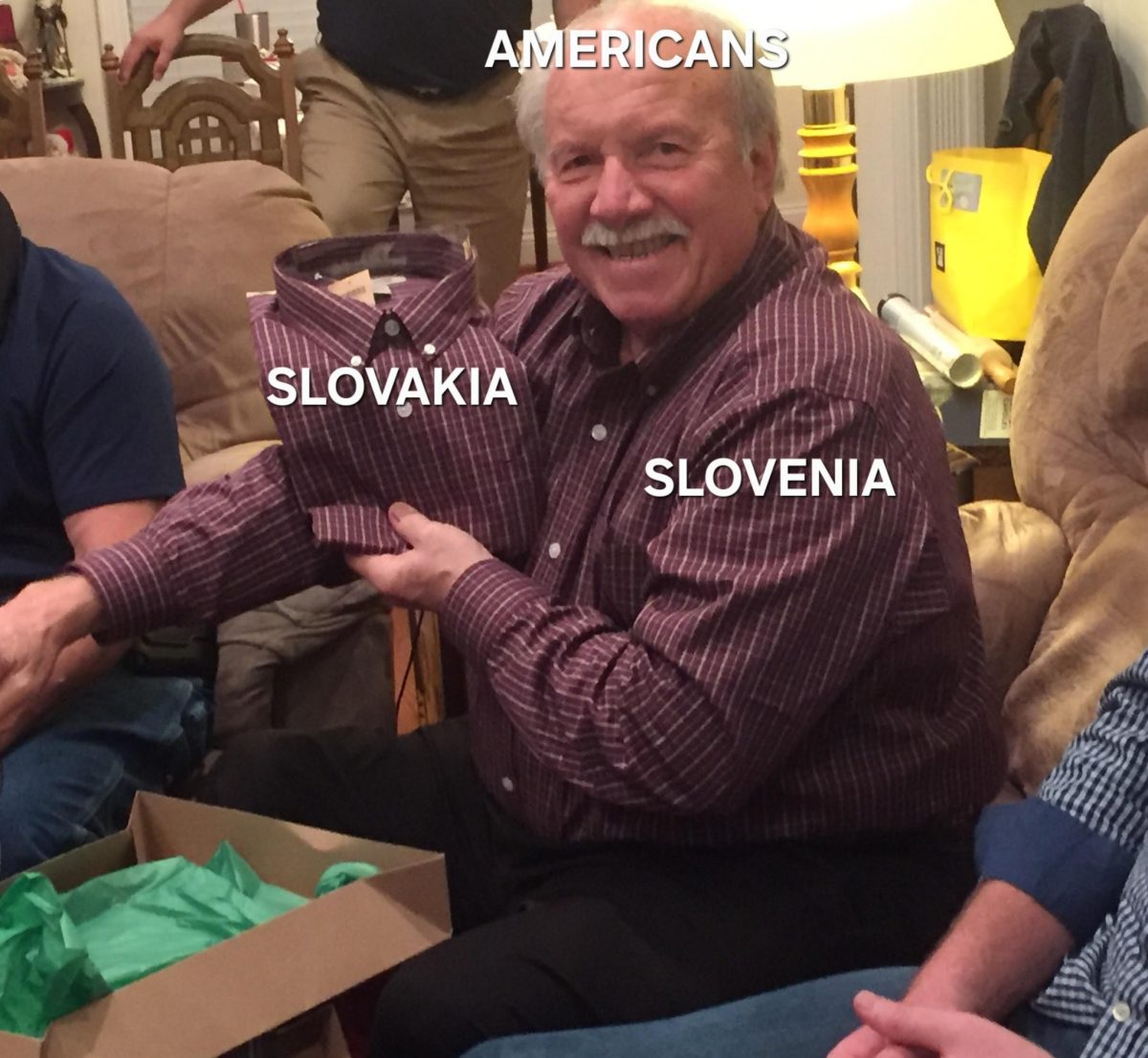 Muž s úsmevom drží košeľu s textom Slovakia, zatiaľ čo jeho vlastná košeľa nesie text Slovenia.