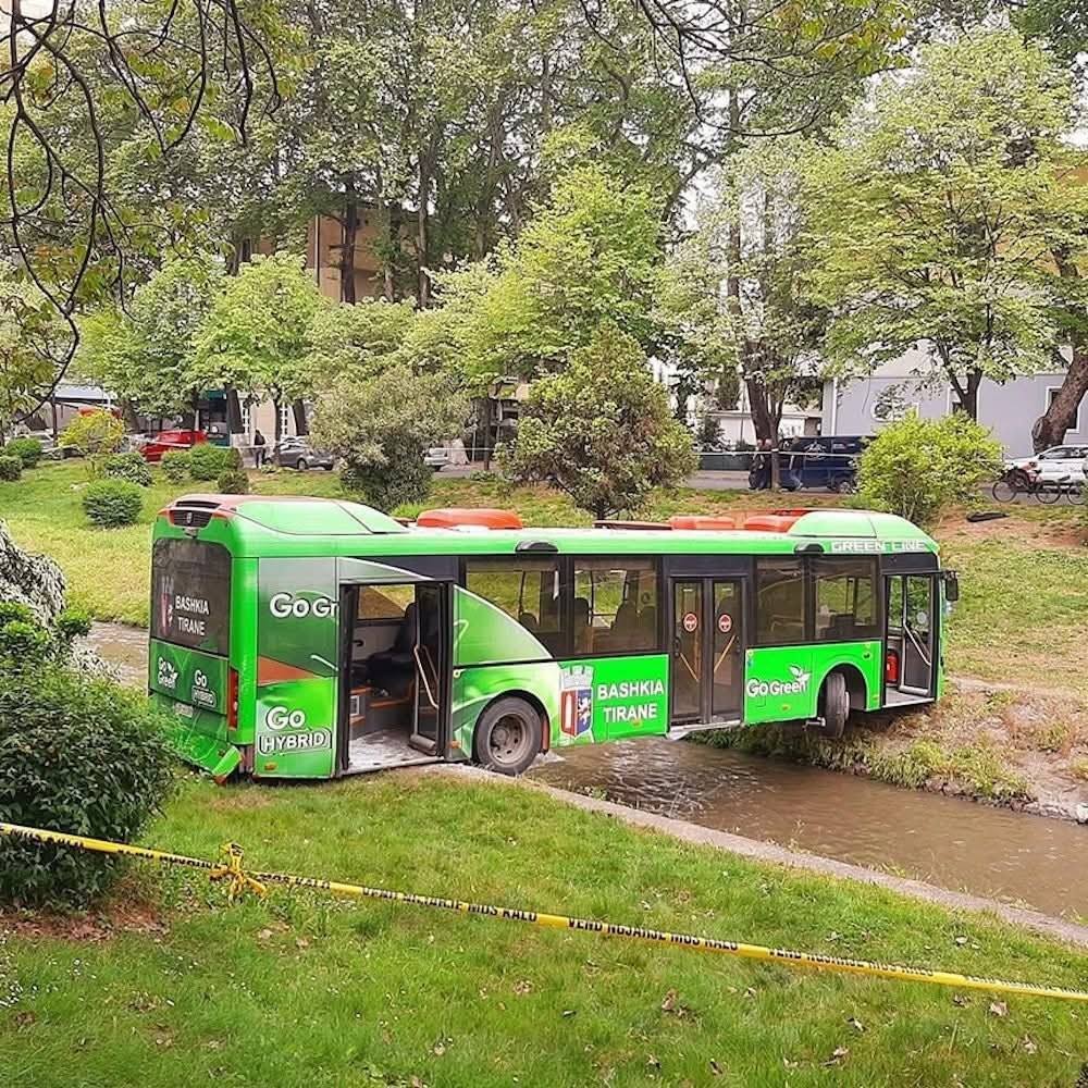Zelený mestský autobus uviaznutý v potoku v parku, obklopený policajnou páskou.