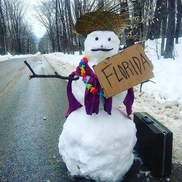 Snehuliak so slameným klobúkom, havajským vencom a tabuľkou Florida stojí pri ceste, pripravený na dovolenku.