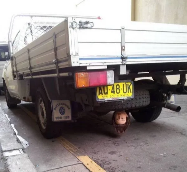 Nákladné auto s bábkovou hlavou na podvozku, zaparkované pri stene.