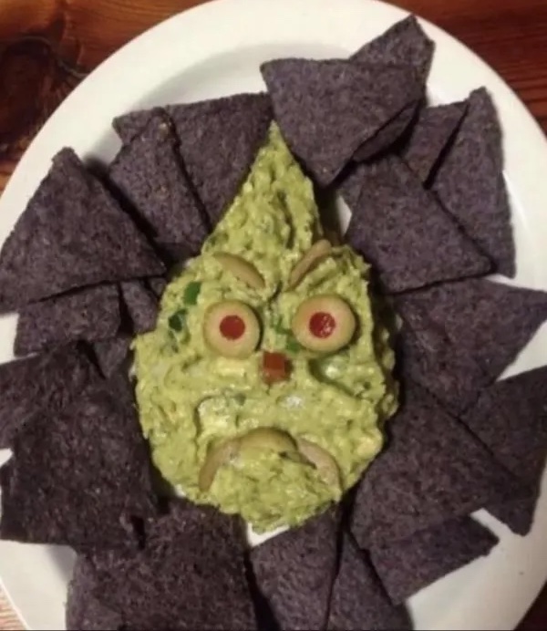 Guacamole v tvare tváre obklopené modrými tortilla čipsmi na bielom tanieri.