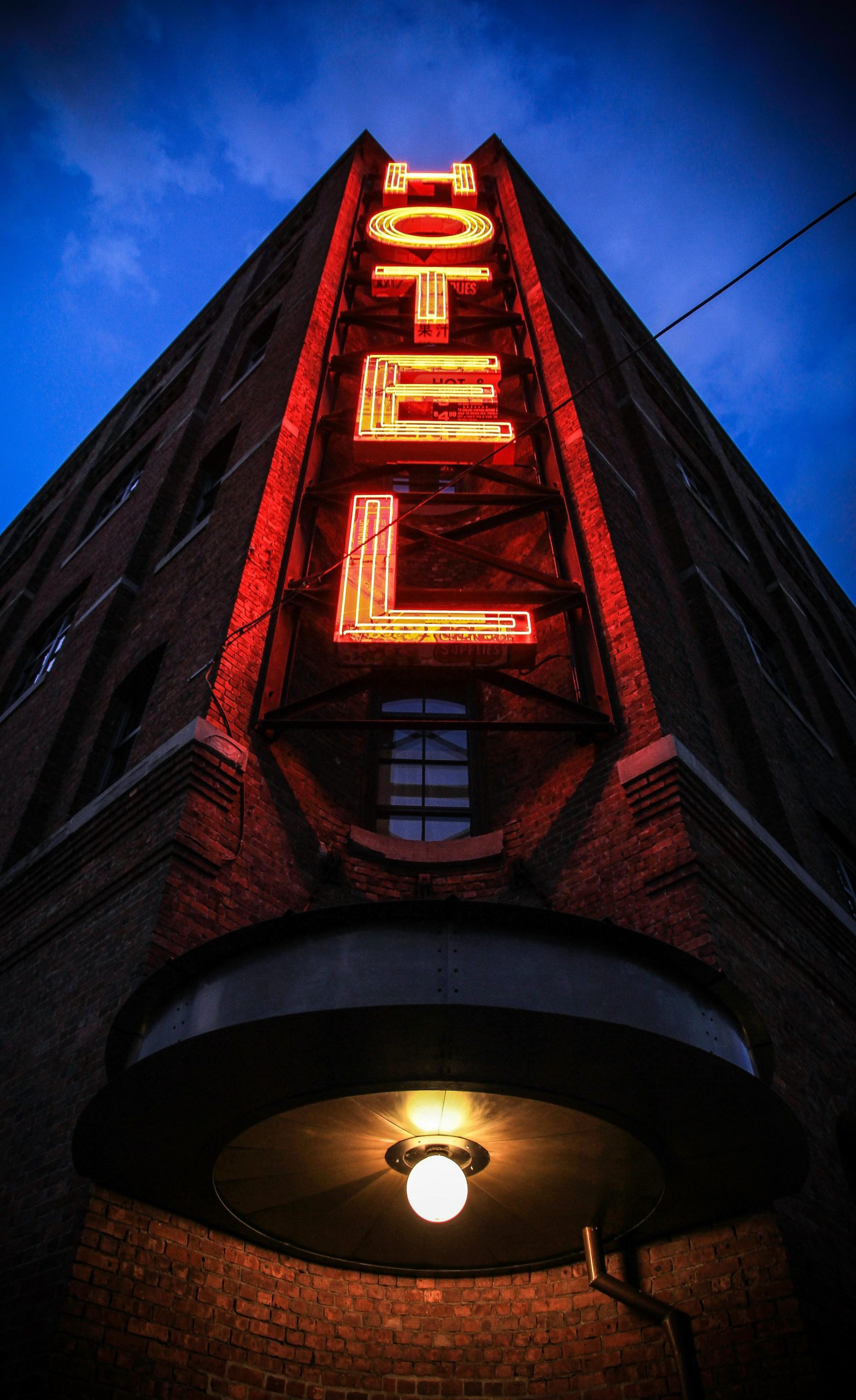 Červený neonový nápis Hotel na tehlovej fasáde večer osvetľuje tmavú mestskú ulicu.