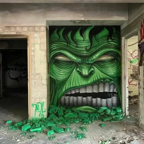 Graffiti zeleného monštra na stene opustenej budovy s rozbitými tehličkami v popredí.