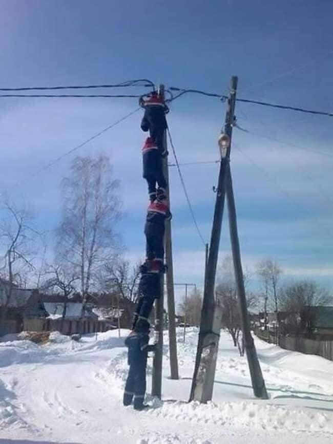 Ľudia tvoria reťaz, aby dosiahli na elektrický stĺp v zasneženej dedine.