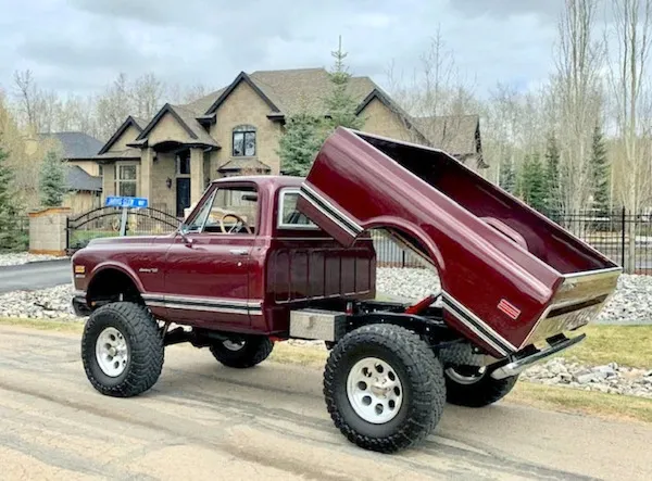Červený offroad pickup s vyklopenou korbou pred vidieckym domom v prírodnom prostredí.
