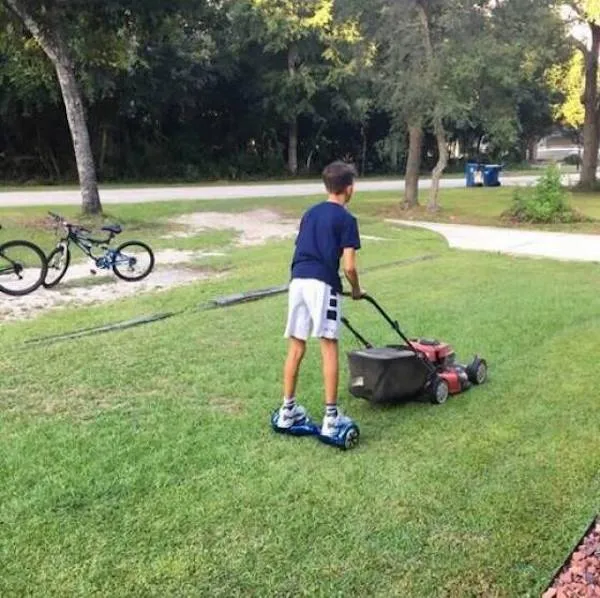 Chlapec kosiaci trávu na hoverboarde na záhrade, vedľa odložený bicykel.