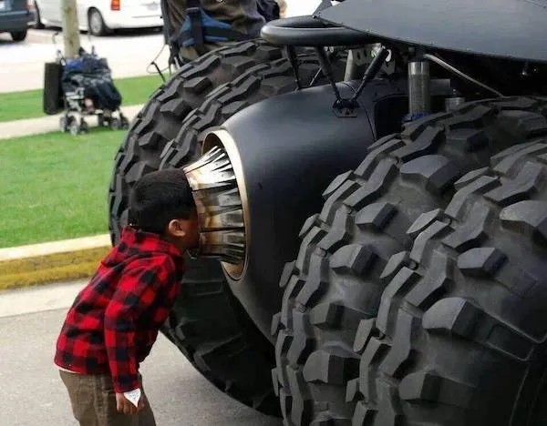 Dieťa skúma obrovskú kolesovú konštrukciu monster trucku na verejnom podujatí.