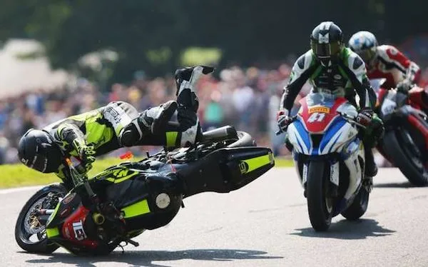 Motocyklový pretekár padá z motocykla počas súťaže, za ním pokračujú ďalší jazdci na trati.
