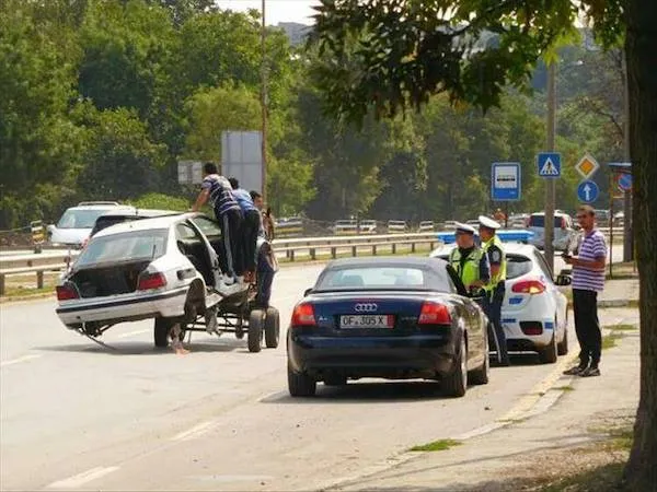 Auto na vozíku na ceste, policajti kontrolujú situáciu, okoloidúci sledujú. Dopravná kontrola pri ceste.