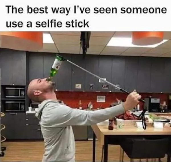 Muž v kuchyni pije z fľaše pripevnenej na selfie tyči v humornom využití.