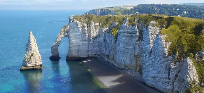 Unikátne biele útesy Etretat vo Francúzsku, obtekajúce tyrkysovým oceánom, s oblúkom a ihlou na obzore.