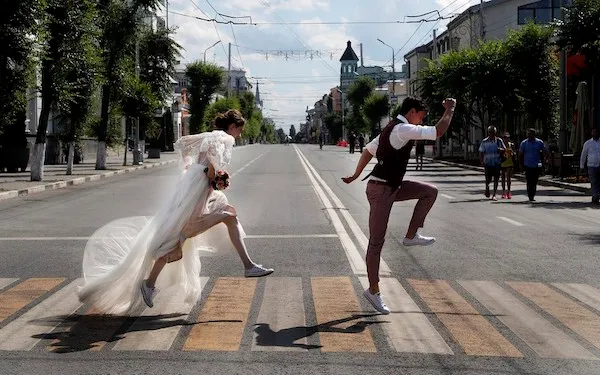 Nevesta a ženích poskakujú po priechode na opustenej ulici v meste za slnečného dňa.