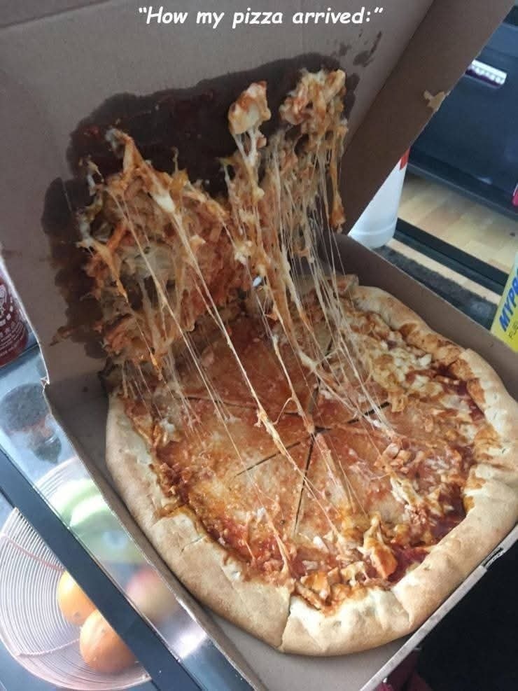 Roztečená pizza v krabici, časť syra a oblohy prilepená na vrchnú stranu, ukazuje nešikovnú prepravu.