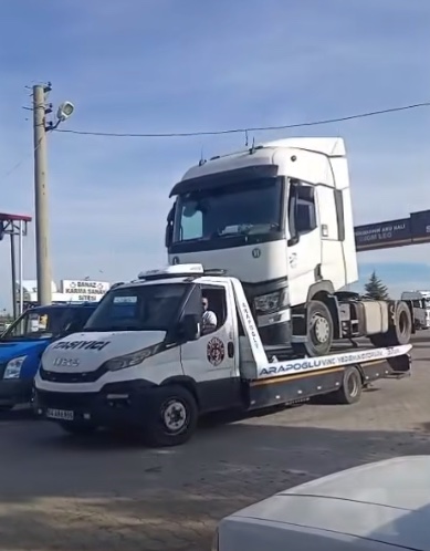 Ťahač na plošine odťahového vozidla na parkovisku za slnečného dňa.