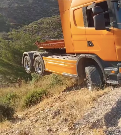 Nákladné auto oranžovej farby zaseknuté na strmom svahu uprostred prírody.