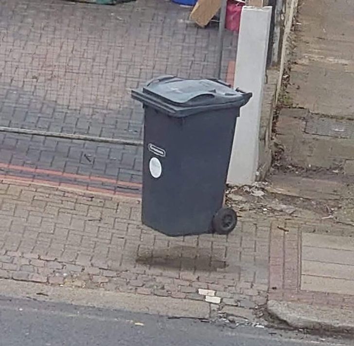 Odpadkový kôš vyzerá, akoby levitoval na chodníku pri ceste.