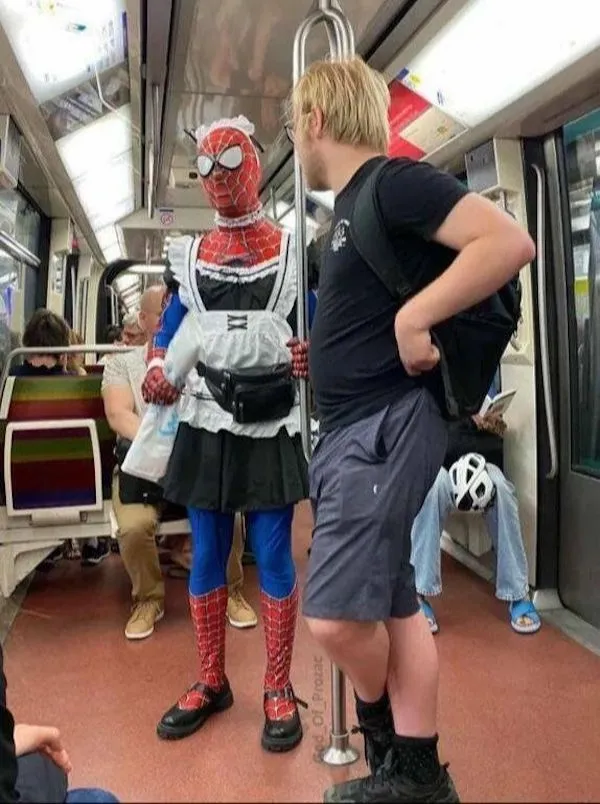 Cestujúci v metre oblečený ako Spider-Man s prekvapivým twistom - slúžkovský kostým, vedľa stojí muž s batohom.