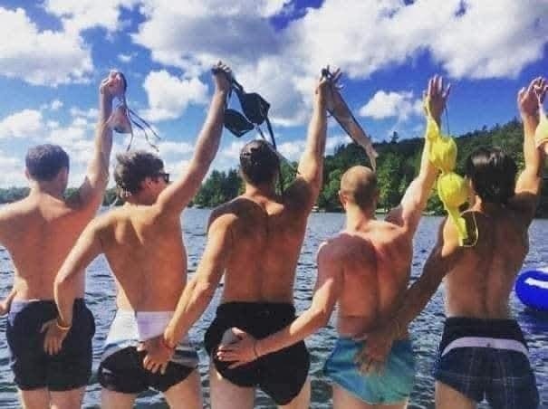 Muži pri jazere držia v rukách plavky, užívajú si slnečný deň pri vode.
