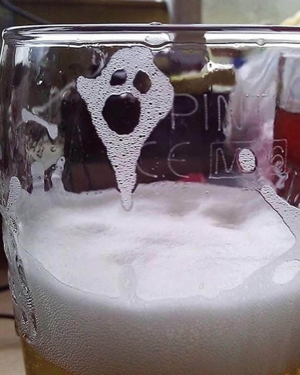 Pivná pena na skle vytvára tvar ducha, pripomínajúci Halloween alebo strašidelnú grimasu.