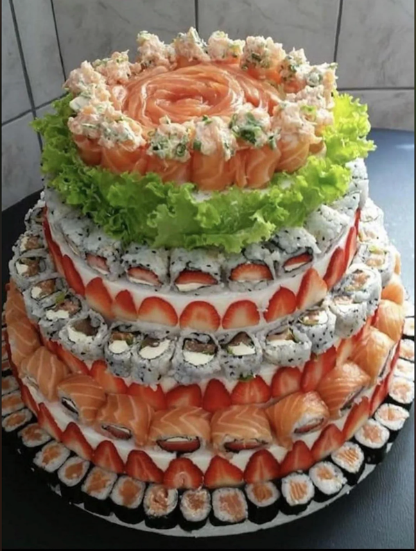 Trojposchodová torta zo sushi, lososa a jahôd, zdobená šalátom. Kreatívna kombinácia sladkých a slaných chutí.