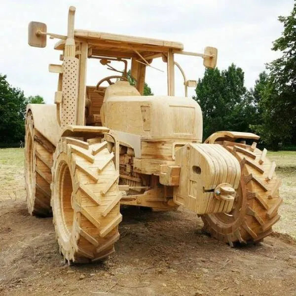 Drevený traktor na poli so zeleným stromom v pozadí, detailná rezbárska práca.