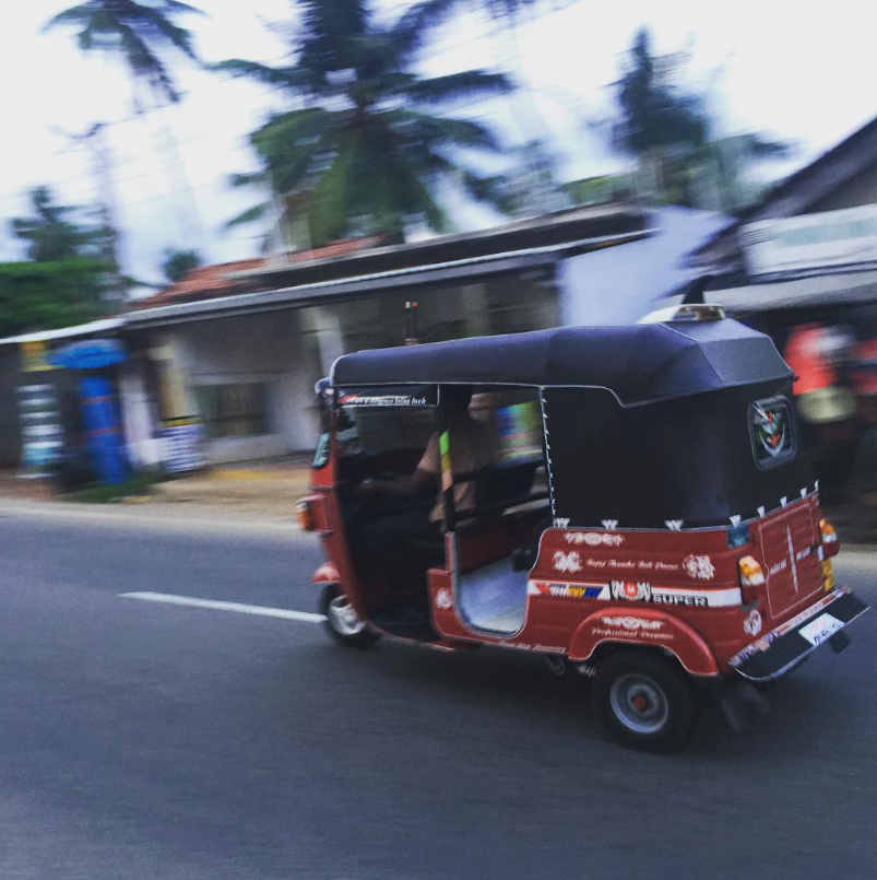 Červený tuktuk jazdí po ulici s palmami v pozadí na tropickom mieste.