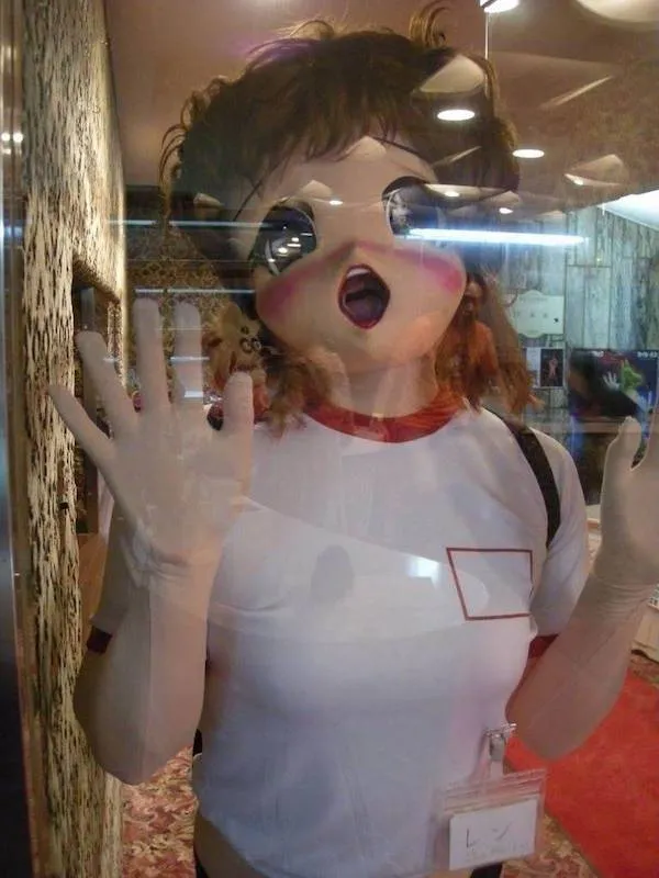 Prepáč, ale neviem, o koho ide na tejto fotke. Tu je alternatívny text: Postava v anime maske za sklom, vzorovaná stena pozadia.