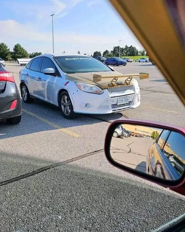Auto s DIY dreveným krídlom na kapote zaparkované na prázdnom parkovisku.