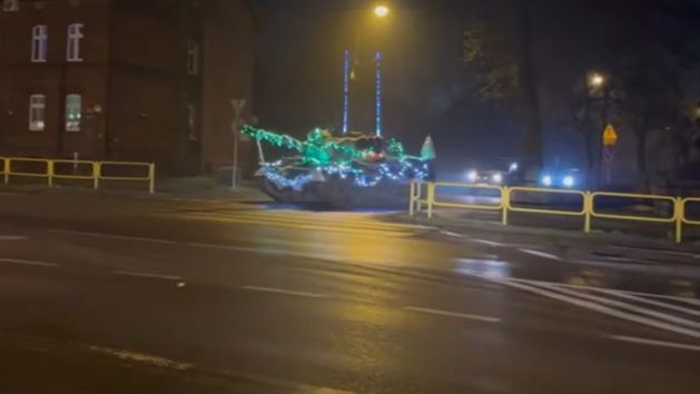 Tank ozdobený farebnými svetlami jazdí v noci po ulici v meste, osvetlený pouličnými lampami.