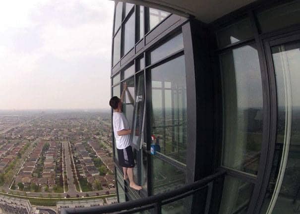 Osoba čistí okná na vysokej budove s výhľadom na mestskú panorámu; výška a bezpečnosť v jednom pohľade.