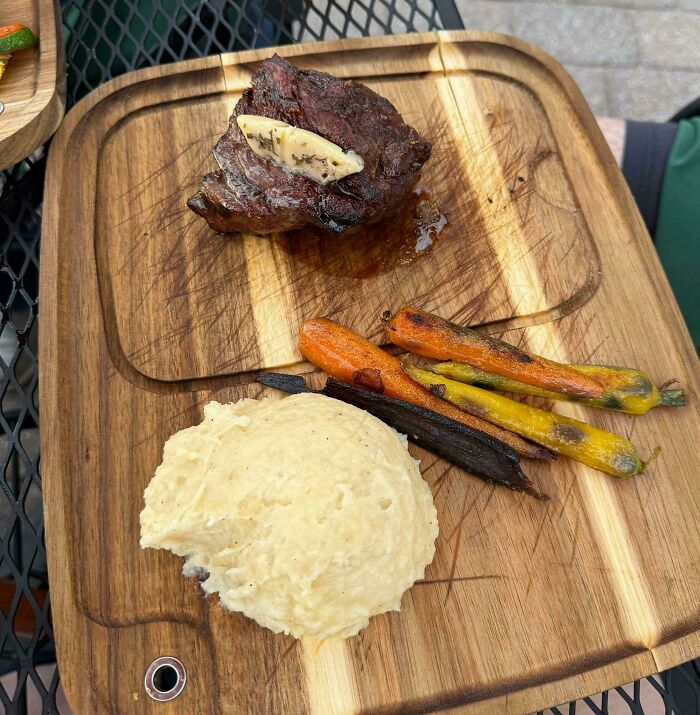 Grilovaný steak s maslom, pečená mrkva a zemiaková kaša na drevenej doske.