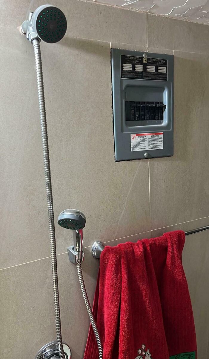 Sprcha so zaveseným červeným uterákom vedľa elektrického rozvádzača na stene.