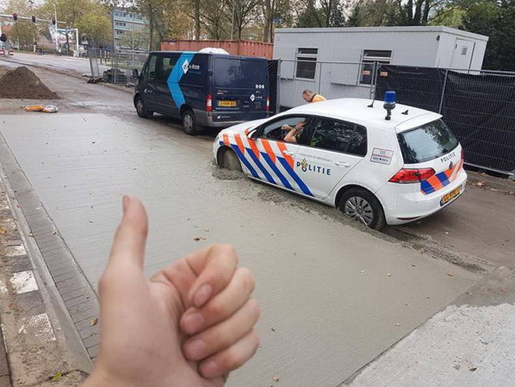 Policajné auto uviaznuté v čerstvom betóne na stavenisku, palec hore v popredí.