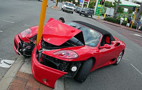 Červené športové auto narazilo do stĺpu na križovatke, poškodená predná časť.