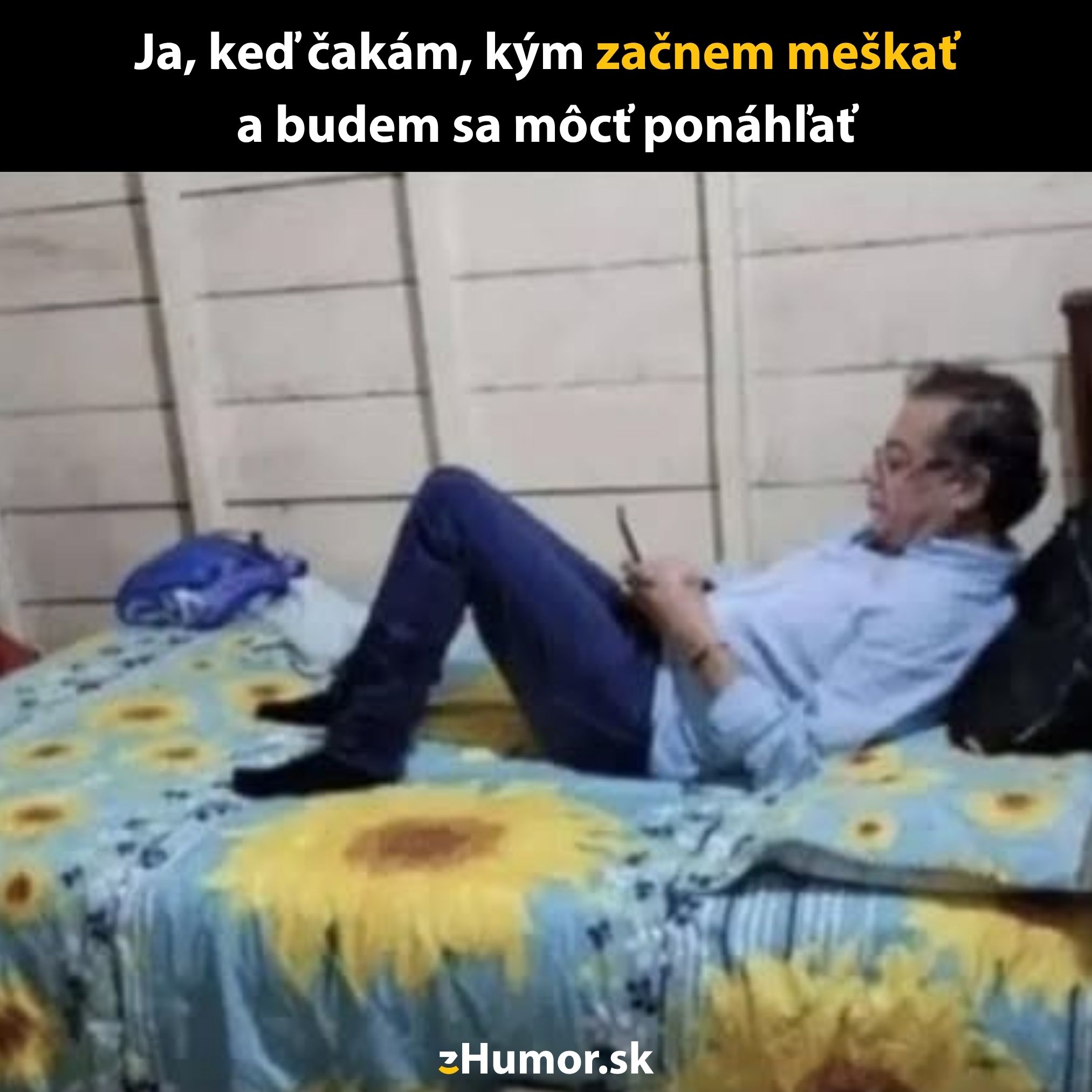 Muž leží na posteli s kvetinovým obliečkami a používa mobil, vtipná situácia o čakaní na meškanie.