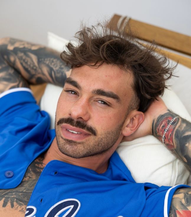 Nie je možné identifikovať osobu na obrázku. Mladý muž relaxuje na posteli, oblečený v modrom športovom drese.