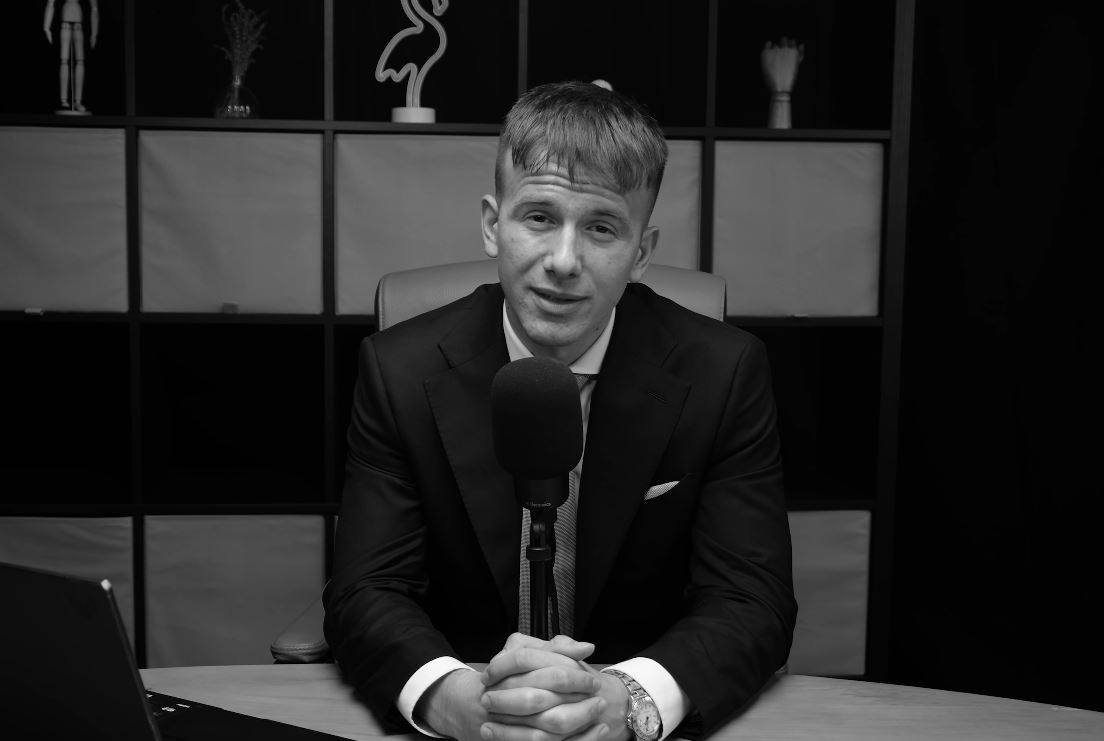 Muž v obleku za stolom s mikrofónom, čiernobiela fotografia v kancelárii.