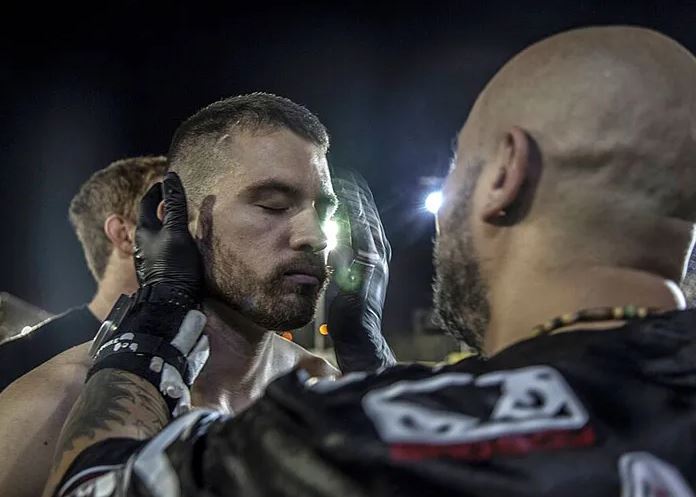 Bojovník sa sústredí pred zápasom, tréner ho motivuje dotykmi na tvári v nočnom osvetlení.