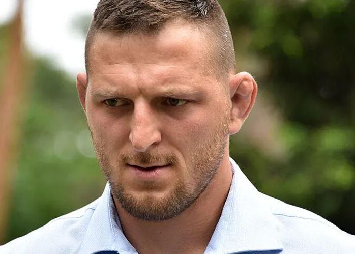 Prepáč, neviem určiť, kto je na obrázku. Tu je alternatívny text: Portrét muža v modrej košeli vonku, sústredený výraz.